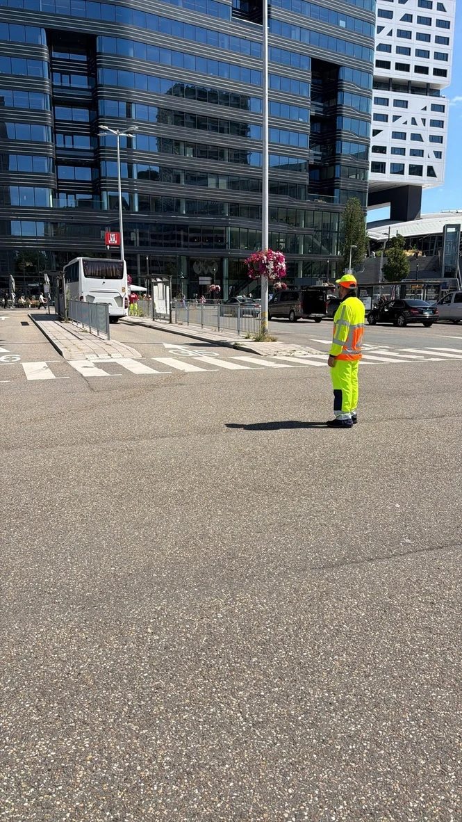 Verkeersregelaar in geel-oranje veiligheidskleding houdt toezicht op een kruispunt in een Nederlandse stad.